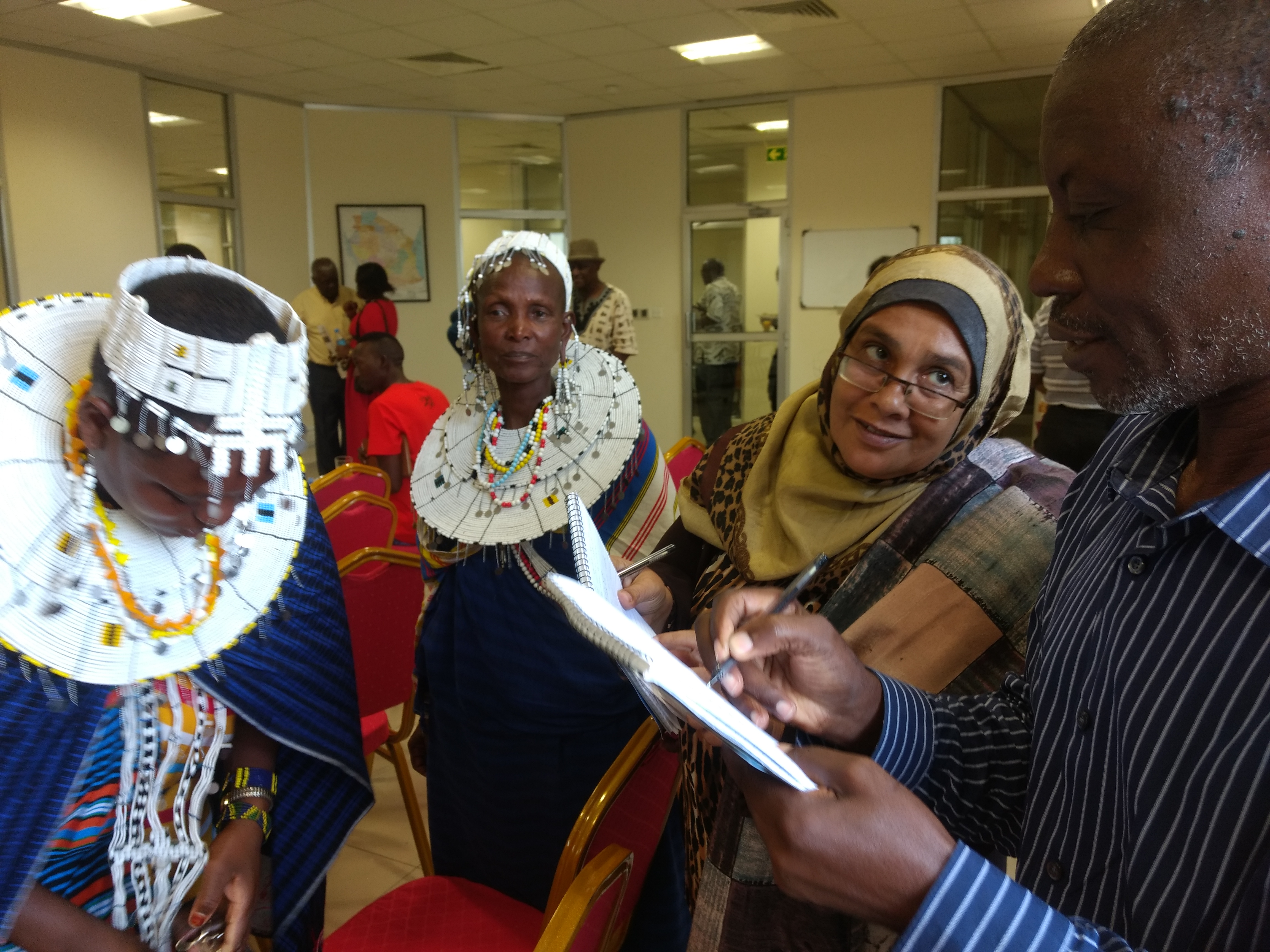 3 women in traditional dress stand with a man who holds a clipboard