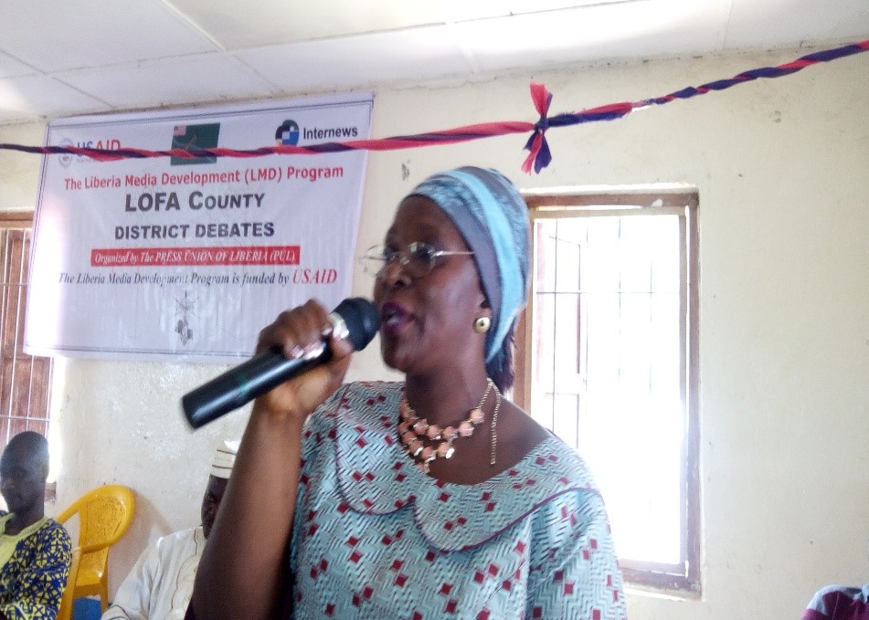 A woman stands speaking into a mic